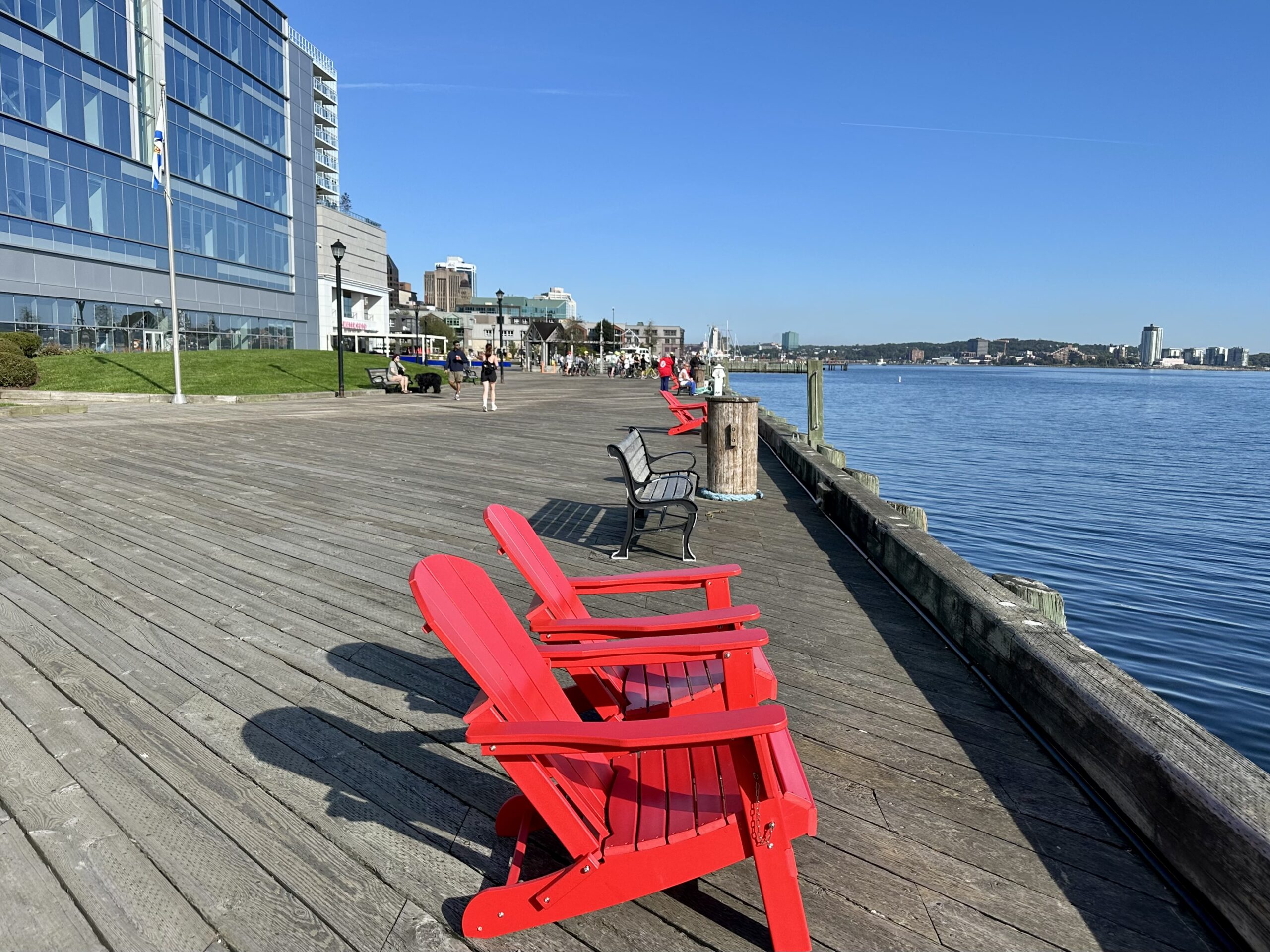 Two red Adirondack chairs on the Halifax boardwalk, a must-see attraction on a Nova Scotia road trip.