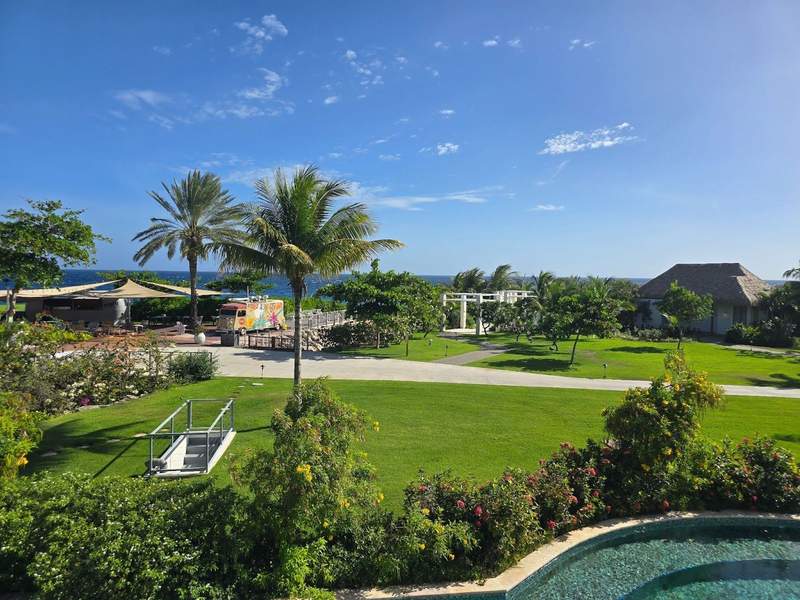Garden-like resort view with green grass, palm trees and blue sky