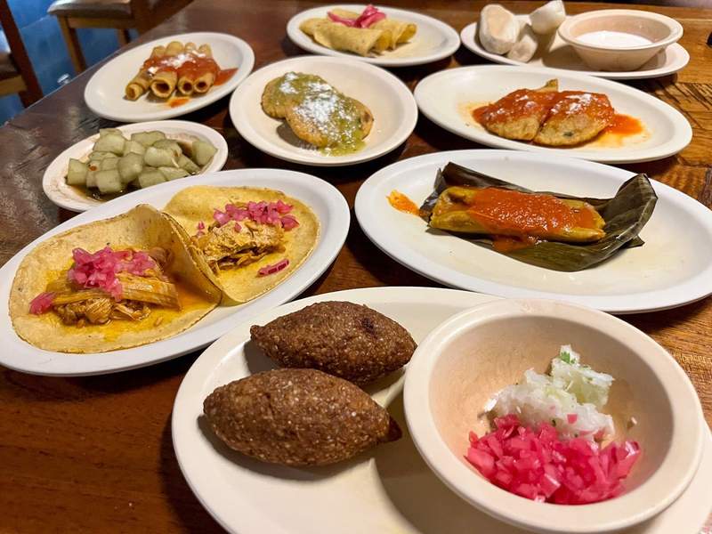 An array of traditional Yucatan snacks, mostly containing corn dough treats and tacos.