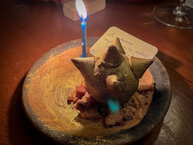 Small cake shaped in the form of a piñata. A candle and a note with a Spanish phrase next to it.