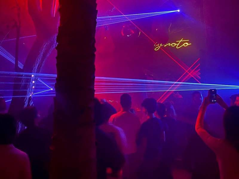 Outdoor night club with red and blue lasers. People can be seen dancing and taking photos.