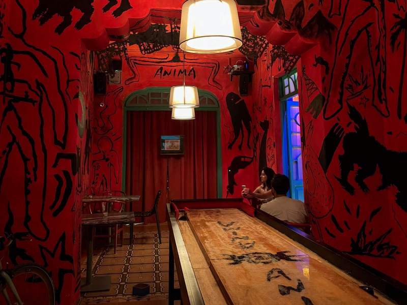 Small room with red walls covered in black scribbles. A shuffleboard table is at the center of the room.