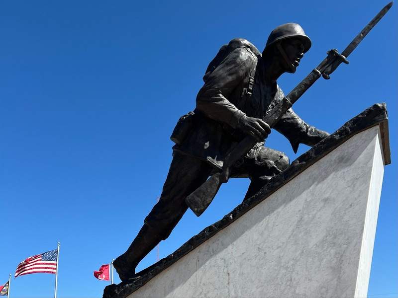 Memorial statue with U.S. flag in background, at Lejueune Memorial Gardens.