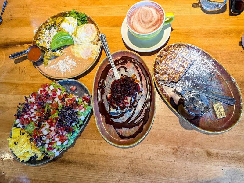 Plates of eggs, avocado toast, and waffles on a wooden table at a brunch restaurant in Reno, Nevada.