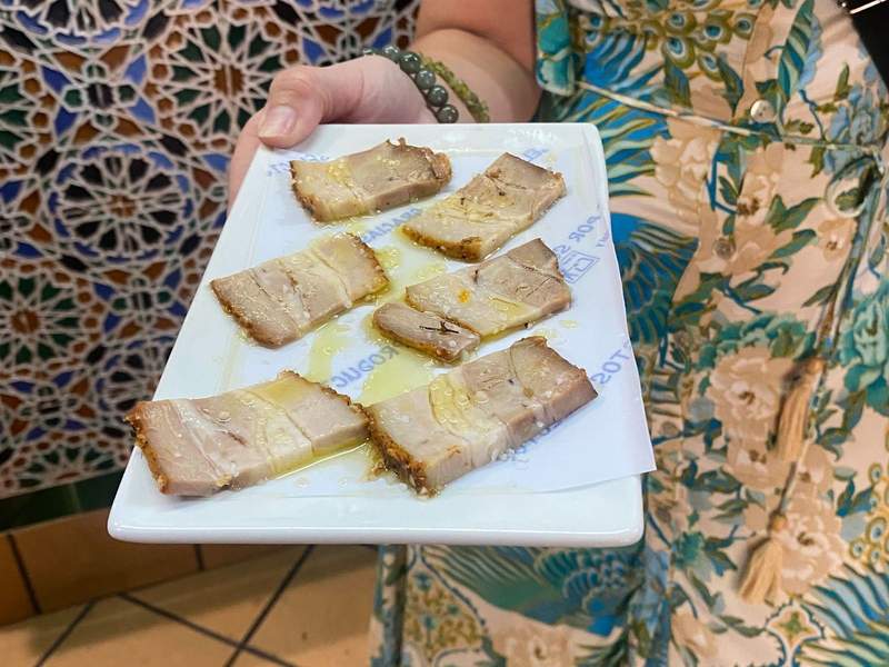 A women holding a a rectangle plate with six small slices of ham.