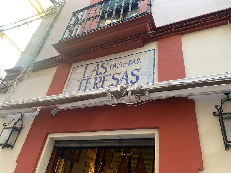 White sign with blue writing and a red boarder, showing an entrance to a bar