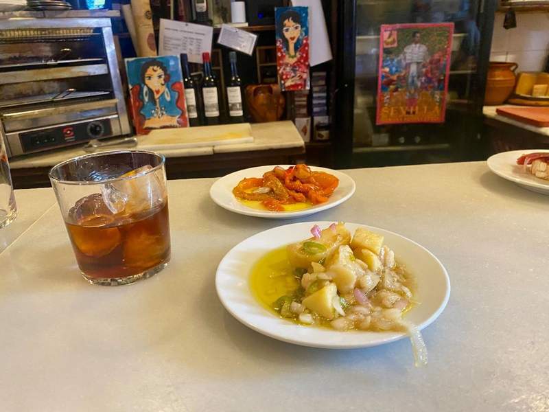 Bar top with a small plate of potato salad and pepper salad with a glass of vermouth