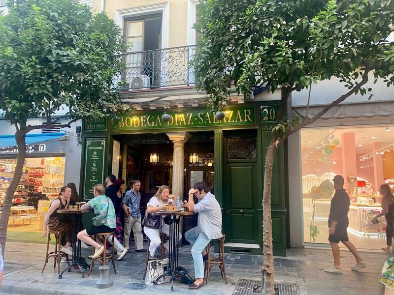 Sidewalk view of the entrance of a bara green doorway and frame. People are sitting at tables outside