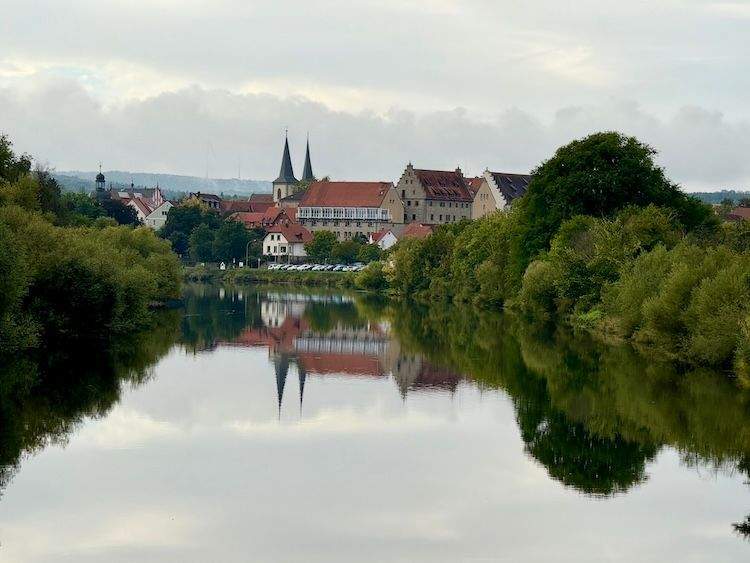Reflection of a red-tiled building with a tall spire in the calm waters of the Danube-Main Canal during a river cruise in Germany.