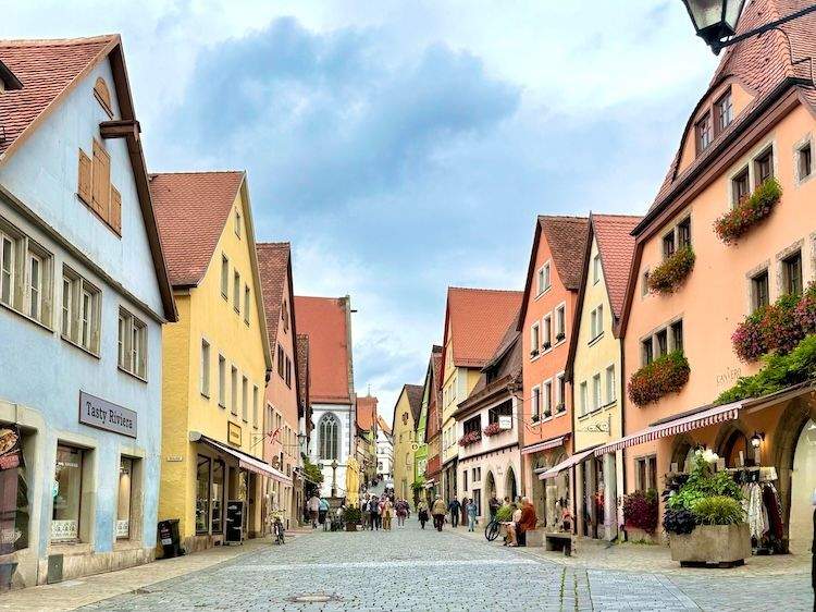 Colorful medieval buildings and shops line a cobbled street in Rothenburg ob der Tauber, Germany.