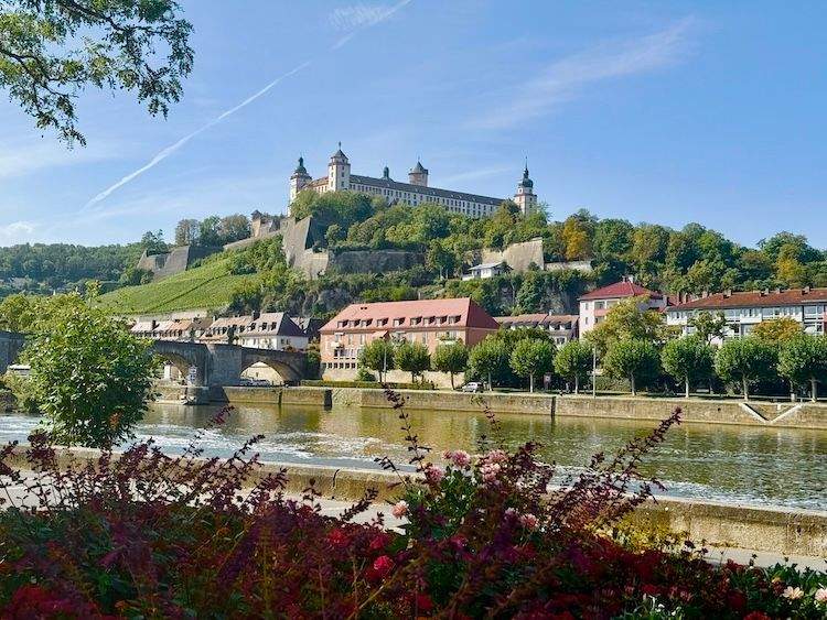 View of Marienberg Fortress overlooking the Main River in Würzburg, with colorful flowers in the foreground.