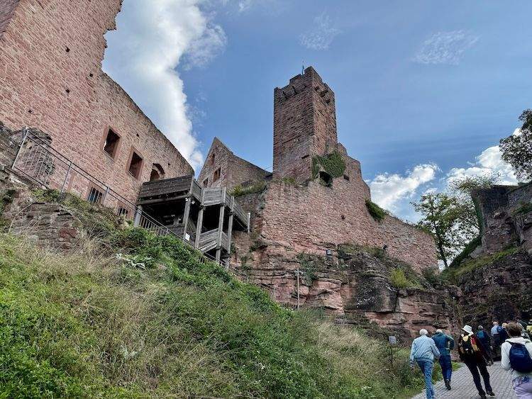 View of hikers approaching the ivy-covered ruins of 12th-century Wertheim Castle overlooking the Main River and town below.