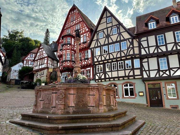 Central square in Miltenberg, Germany, with half-timbered houses and a medieval stone fountain.