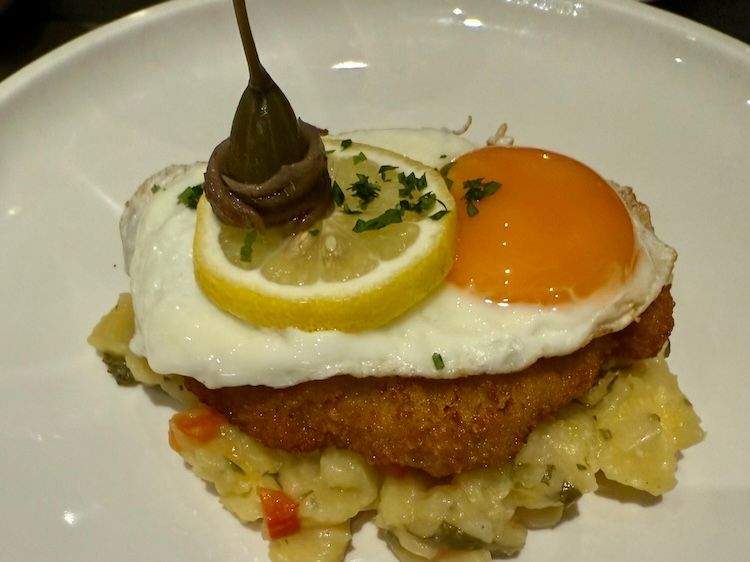 Plate of Holstein Schnitzel topped with a sunny-side-up egg, served over German potato salad.