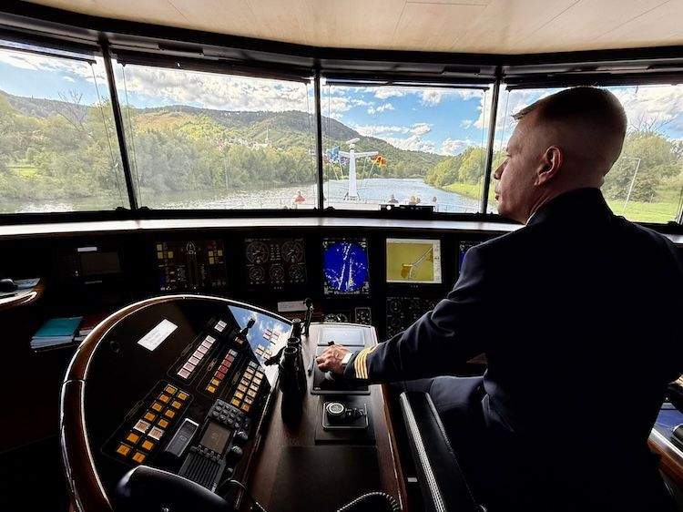 Captain Bálint Paricsi seated in the wheelhouse of the MS George Eliot, looking out over the river through front-facing windows.
