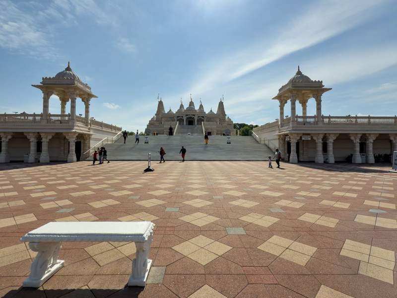 Front entrance of BAPS Shri Swaminarayan Mandir in Atlanta with intricate white marble carvings, arched doorways, and soaring spires under a bright blue sky.