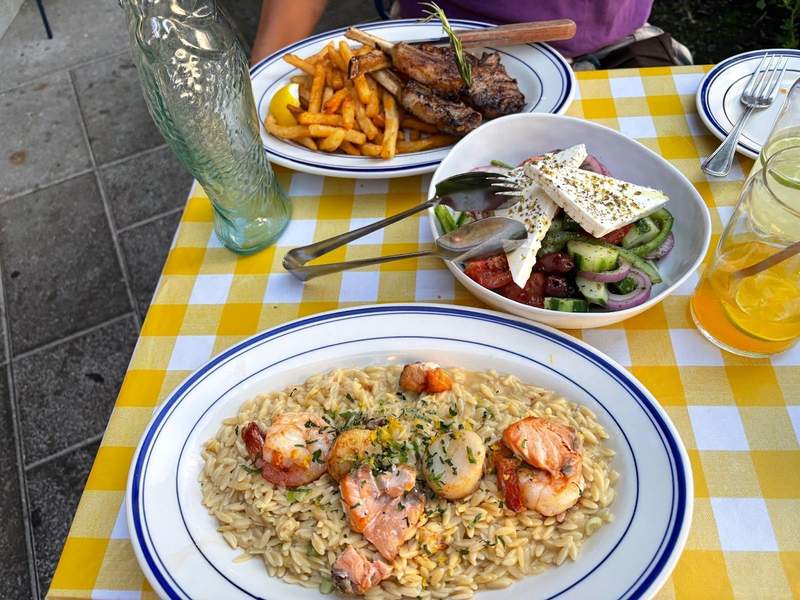 A couple's date night dinner of seafood orzo, lamb chops with french fries, and Greek salad with feta and veggies at Psaraki in Brooklyn, NYC.