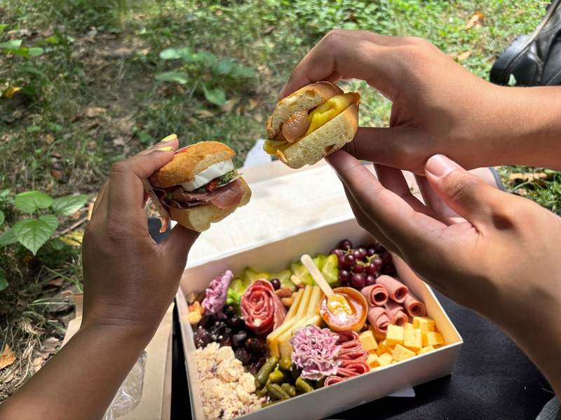 A couple sharing a romantic picnic with a charcuterie board and sandwiches in Central Park.