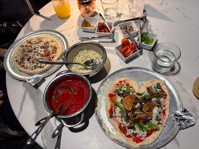 A couple's pizza making brunch with toppings like mushrooms, potatoes and peppers. A tin of cheese and sauce and pizzas on trays in the shape of a heart at Adoro Lei.