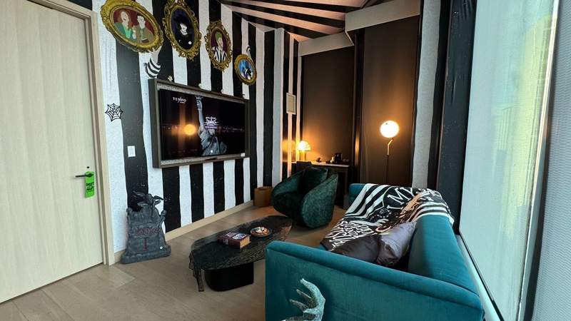 black and white striped wall paper with character images, a green sofa, coffin shaped coffee table at the Beetlejuice suite.