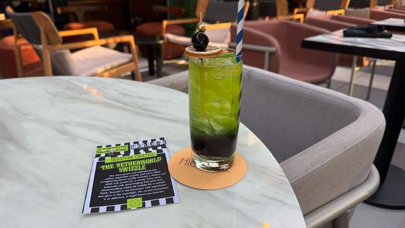 Green and black beverage in a glass next to a promo card at the Tempo by Hilton New ork Times Square.