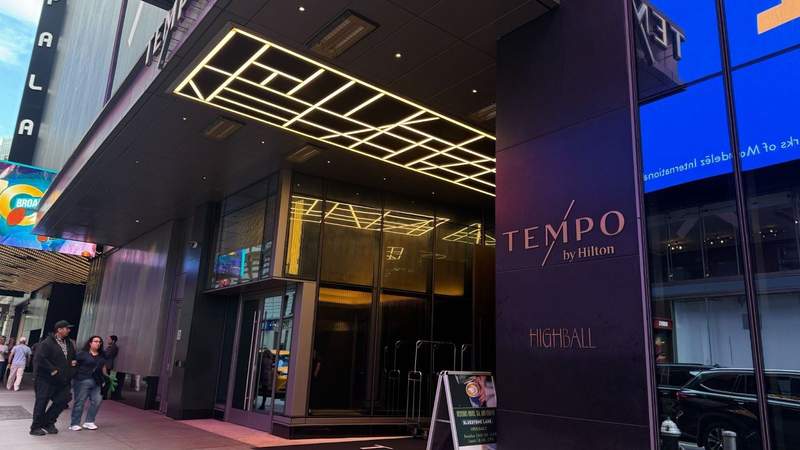Black entrance sigh with gold text that reads Tempo by Hilton next to glass panels.