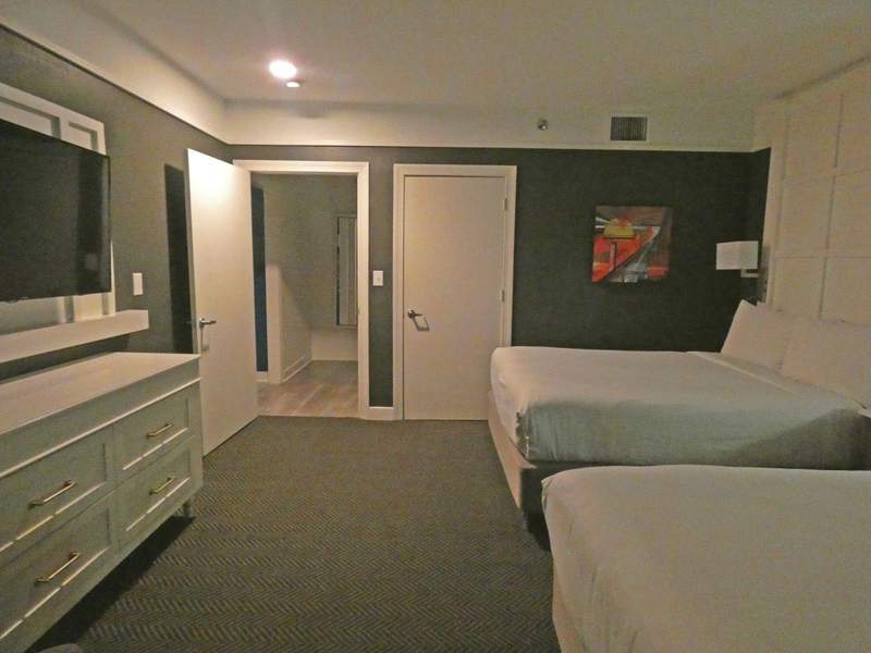 A hotel suite with two beds and dresser.