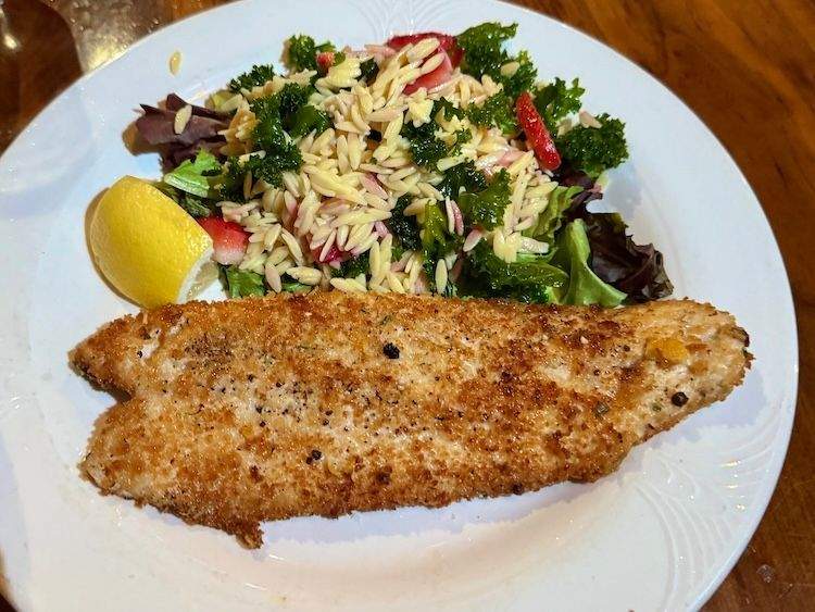 A plated serving of pan-seared trout at Enoteca in Ketchum, Idaho, garnished with herbs and accompanied by seasonal vegetables.