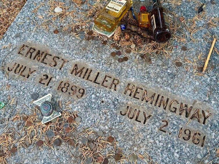 Gravesite of Ernest Hemingway in Ketchum Cemetery, adorned with personal mementos left by visitors, including coins, pens, and small bottles.