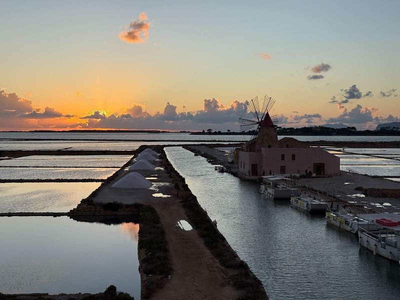 The Saline di Marsala salt flats at sunset with a windmill in the distance.
