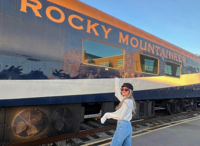 Woman poses by the exterior of the iconic Rocky Mountaineer train.