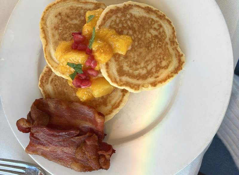 A plate of lemon buttermilk pancakes with fruit compote sits next to bacon on a plate.