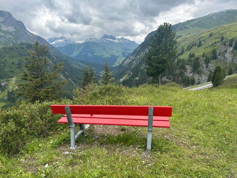 A red bench looking out at the mountain peaks on a hiking trail in the Arlberg region of the Austrian Alps. 