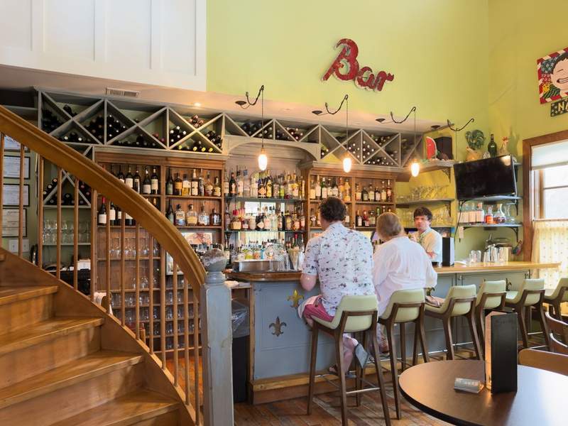 Bar at The Flying Melon on Ocracoke lined with wine bottles and cocktail garnishes; guests enjoying seafood plates.