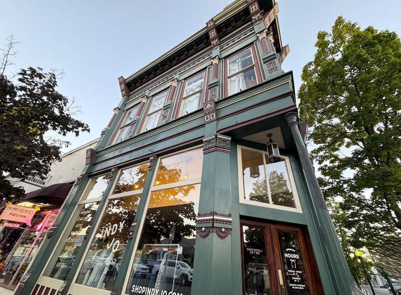 Victorian style green with maroon highlights building in Grants Pass, Oregon. Lower floor has large windows.