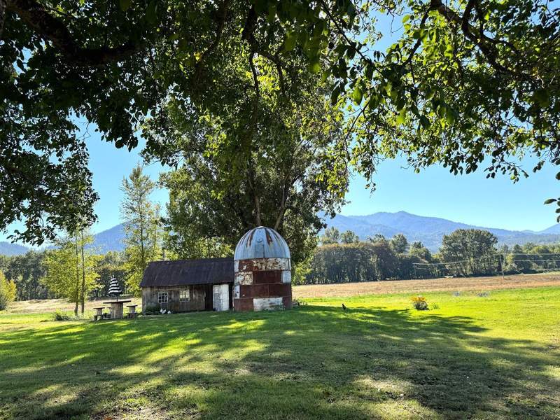 Beautiful farm visita with mountains in the background, a small barn and lush, green trees.