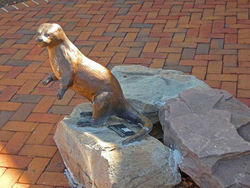 Statue of an otter on rocks against a brick walkway.