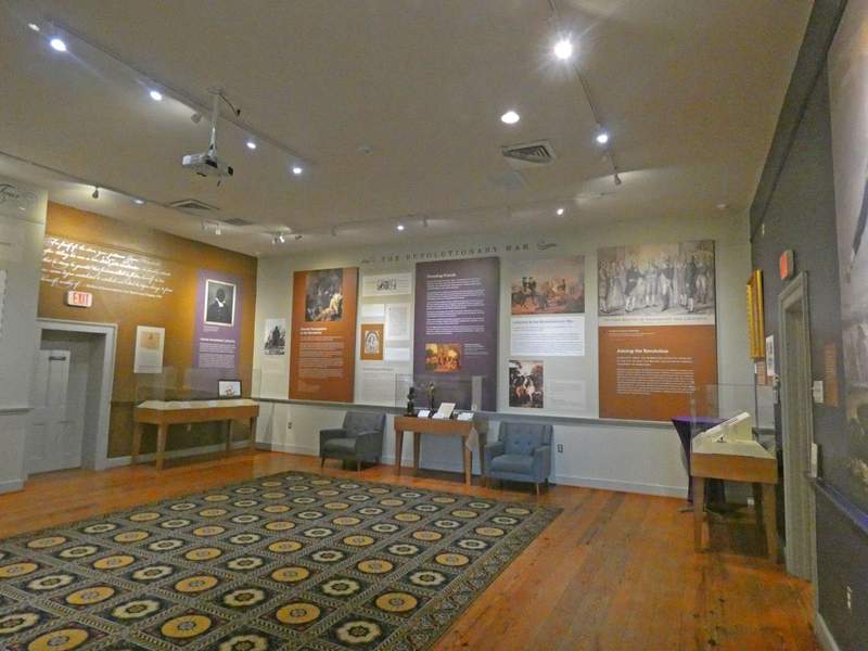 A museum exhibit with posters and artifacts around pale green walls and a rug on a hardwood floor.