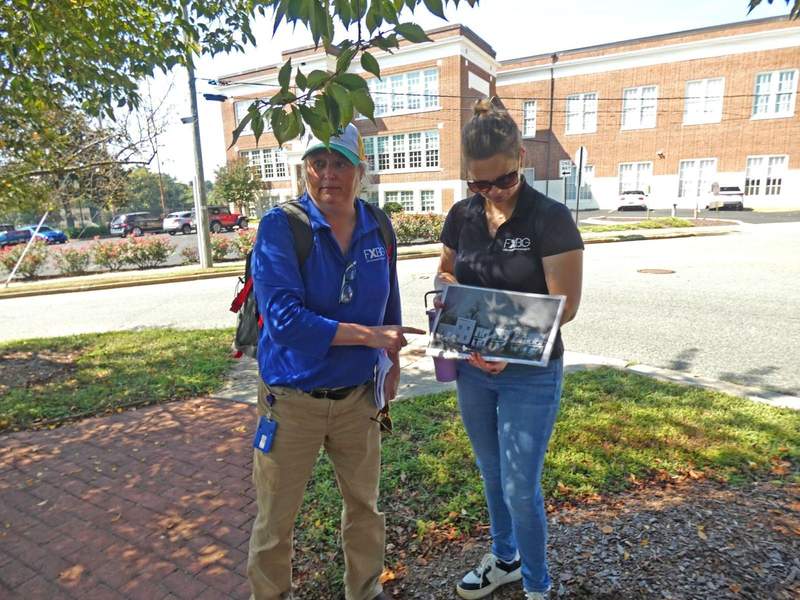 Two women talking a bout a photograph in front of a red brick former school.