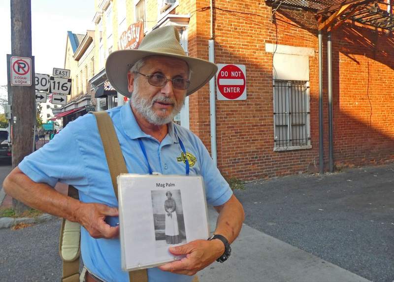 A man standing in front of an alley holding a picture of a Civil War era Black woman.