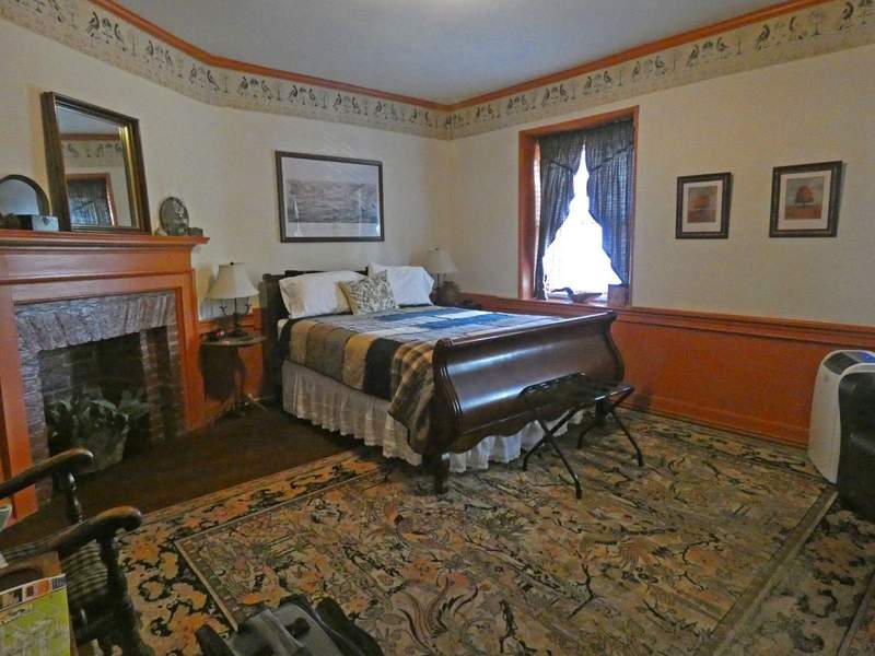 A civil war era bedtoom wiht fireplace and bed next to window.