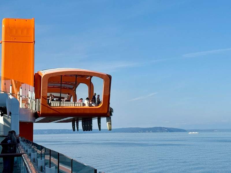 The bright orange Magic Carpet extends from the side of the Celebrity Edge Cruise ship. Views of the Puget Sound in the background.