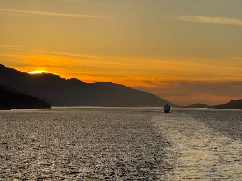 A cruise ship surrounded by mountains as the sun sets.