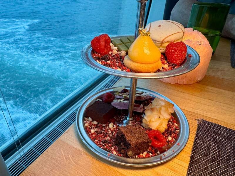 Tiered tray with yummy treats including brownies, candy, macarons,  and raspberries on a bed of sprinkles.