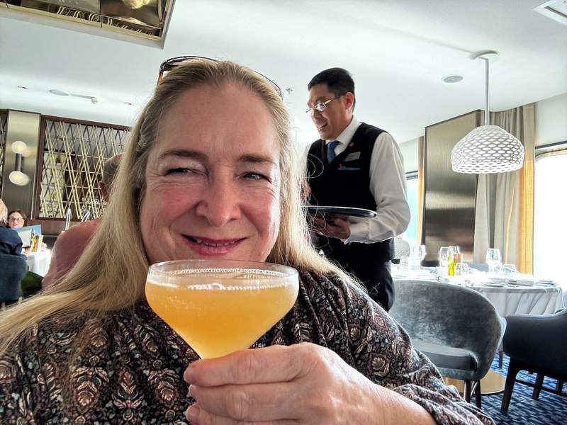 Lady sips on a cocktail in a dining room, waiter in the background