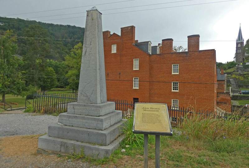 Gray stone monument with placard and red brick house in background