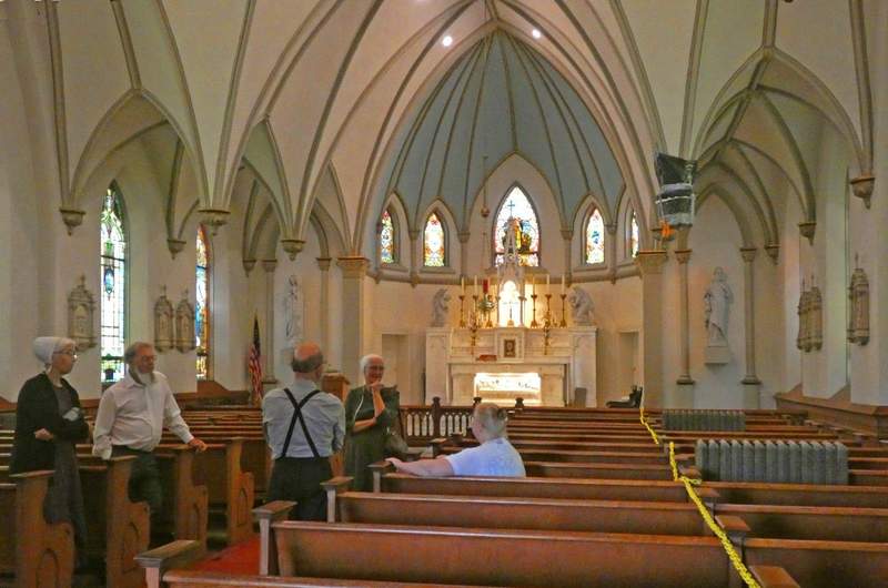 Interior of a church with white altar and tall domes with several people in pews.
