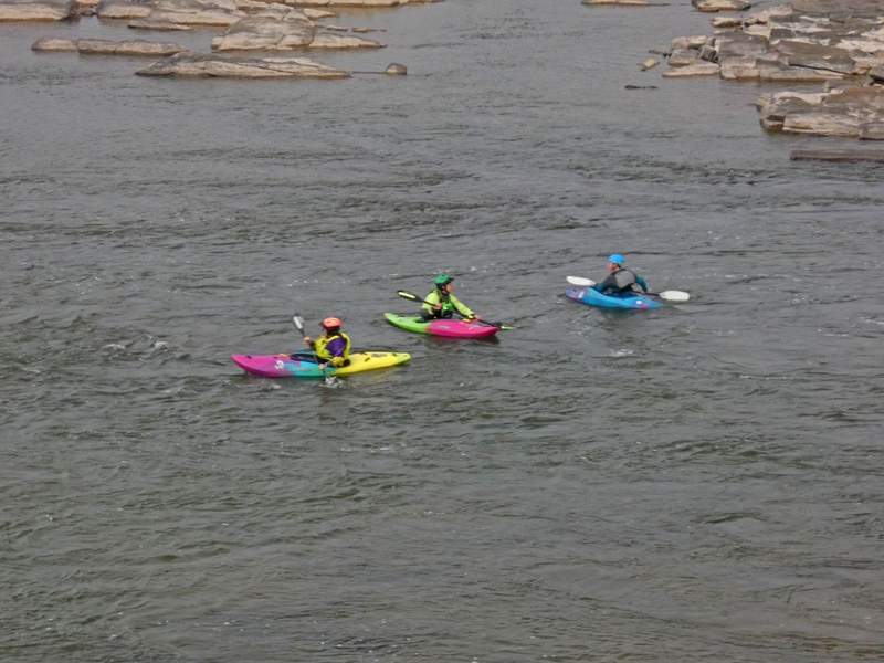 Three kayakers in brightly colored kayaks in river.