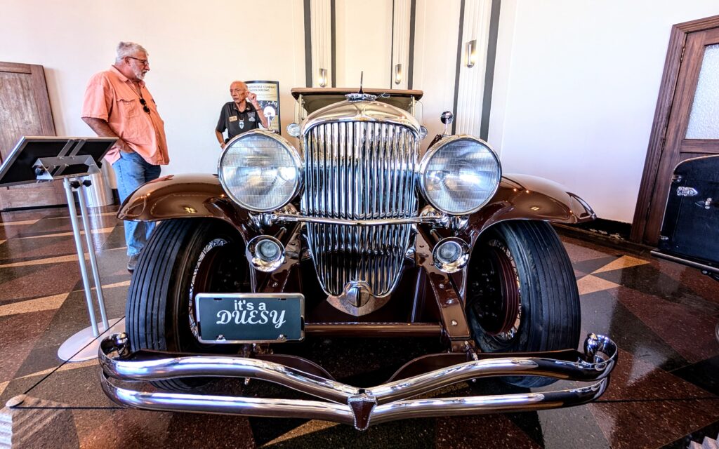 two men standing next to a Duesenberg car