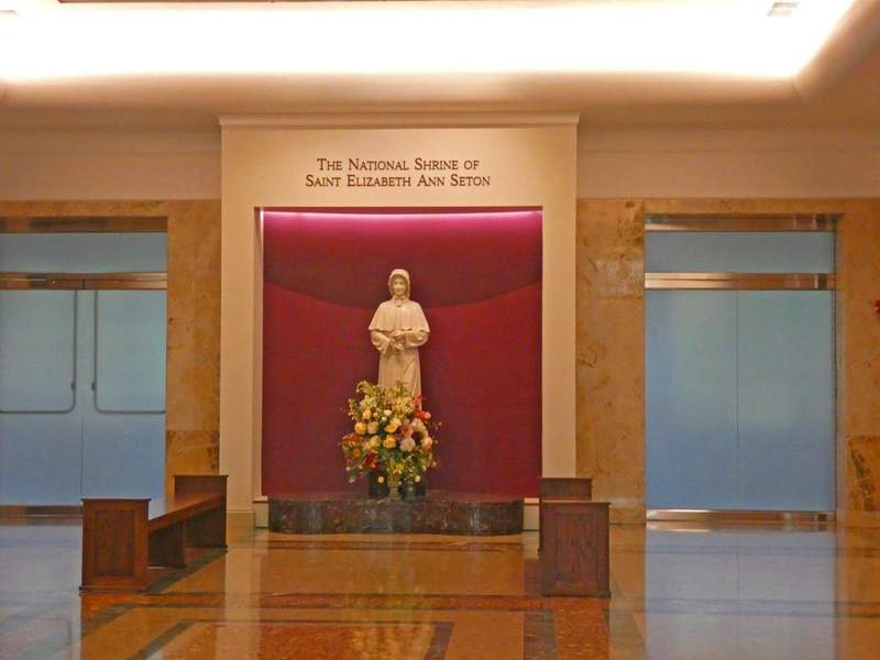 A statue of a woman in nun's habit with a magenta colored background bordered by doors on each side.